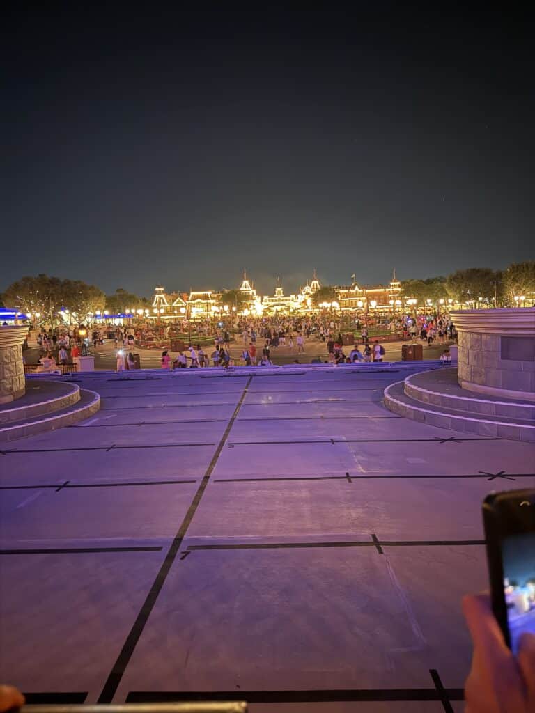 Night view of Magic Kingdom entrance and Main Street, U.S.A. train station area, with crowds and bright lights as guests exit the park.