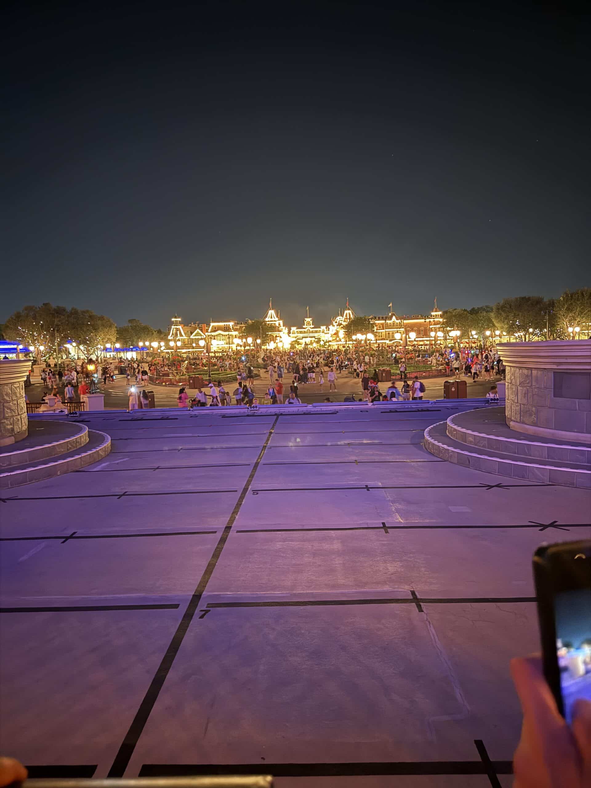 Night view of Magic Kingdom entrance and Main Street, U.S.A. train station area, with crowds and bright lights as guests exit the park.