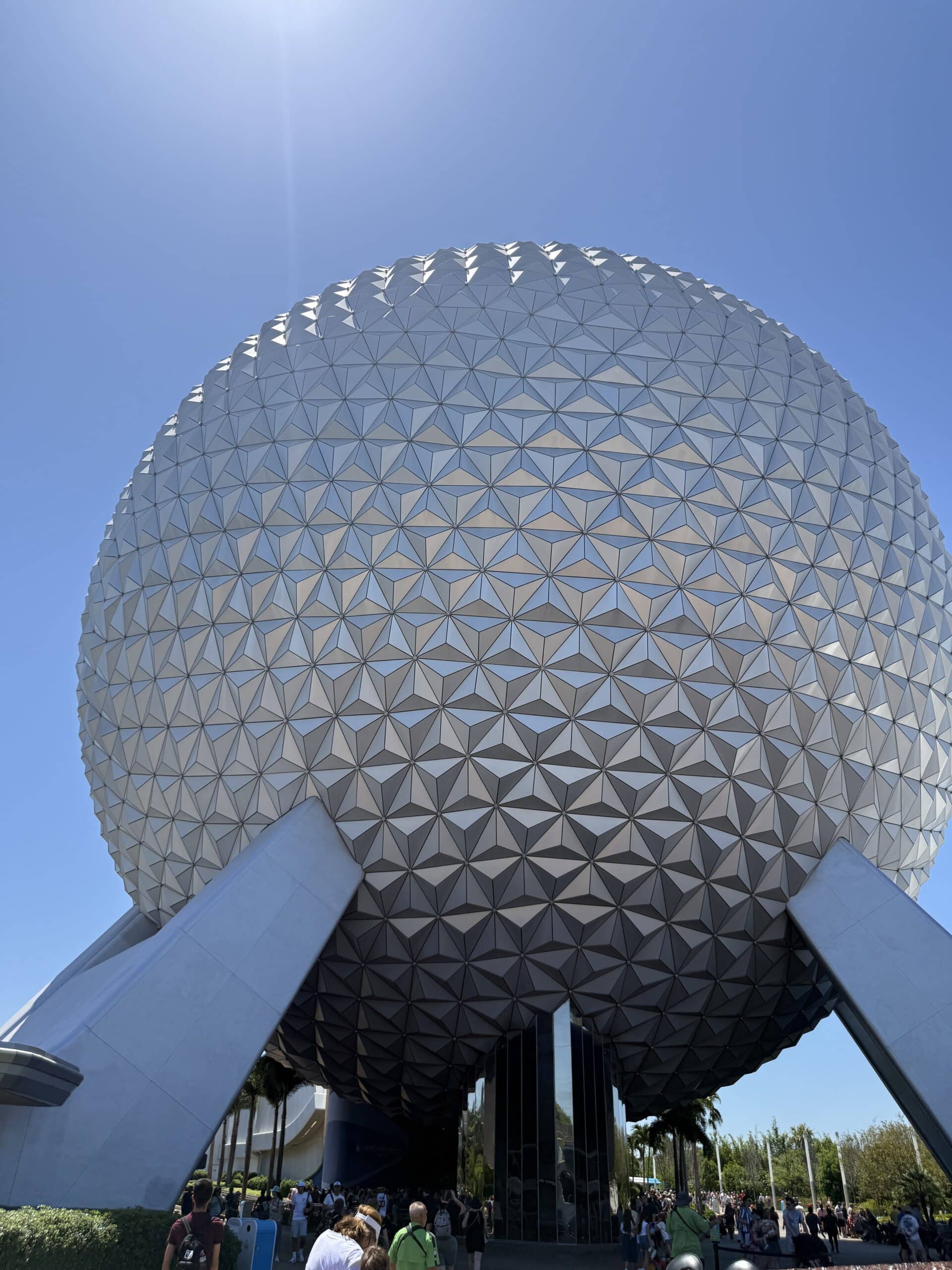 Close-up view of the geodesic sphere at EPCOT in Disney World, showing its triangular metallic panels and supporting legs against a clear blue sky.