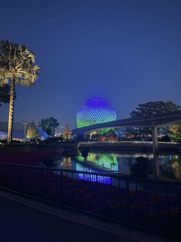 Spaceship Earth reflecting in water at night at EPCOT in Walt Disney World with colorful LED lighting