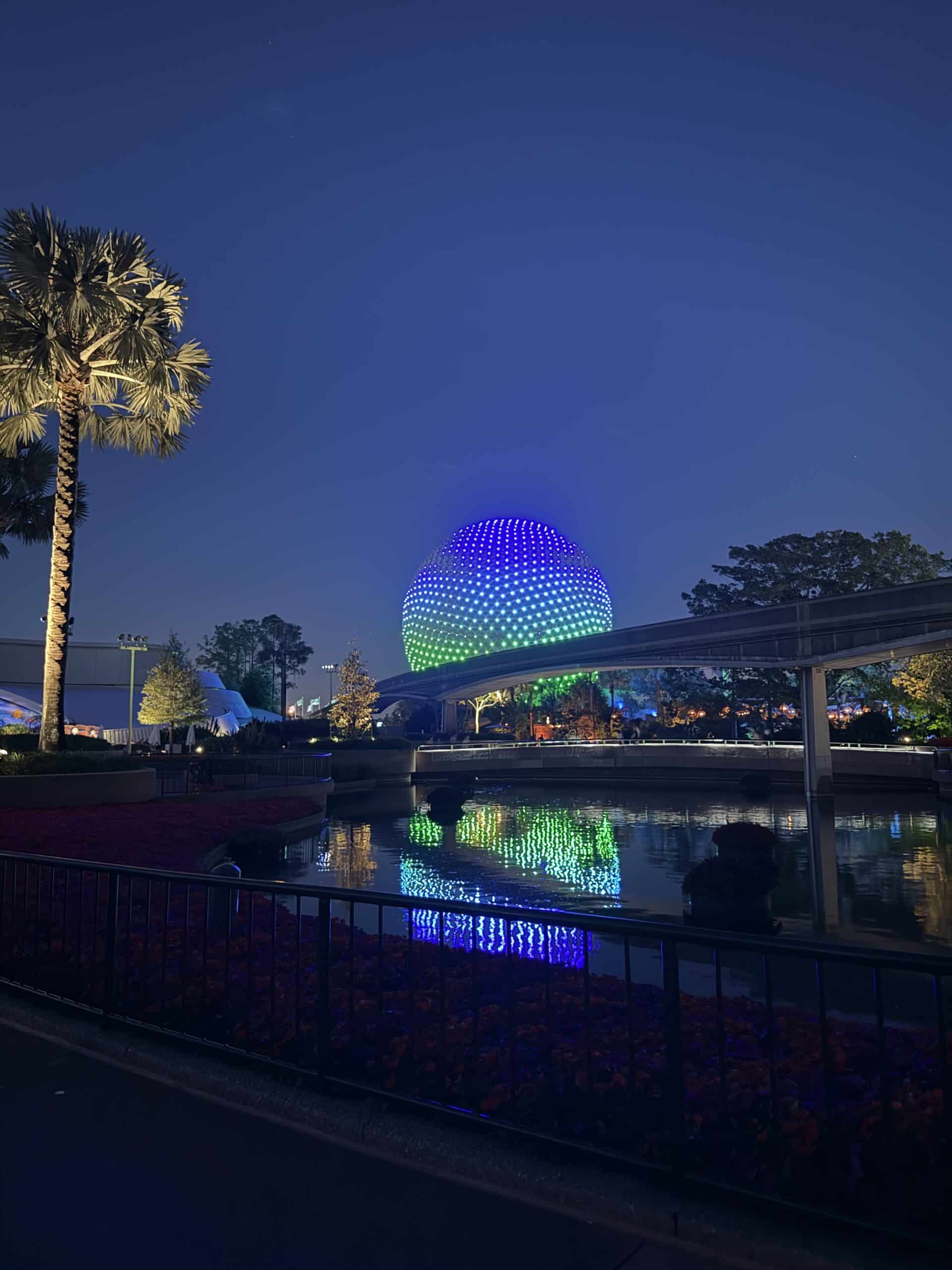 Spaceship Earth reflecting in water at night at EPCOT in Walt Disney World with colorful LED lighting